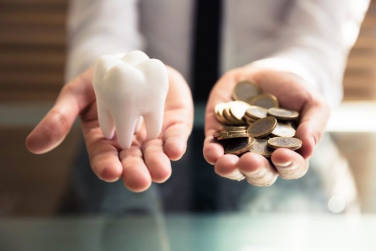 Two hands holding a large tooth in one and coins in another